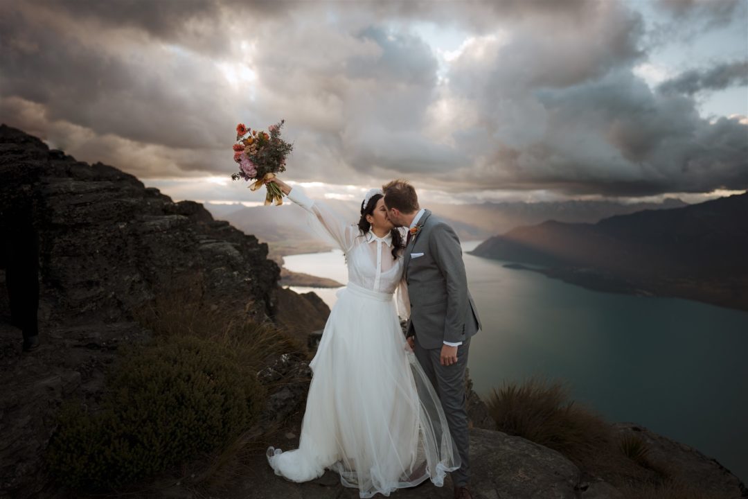 just married couple kiss and celebrate on mountain top in Queenstown New Zealand at sunset