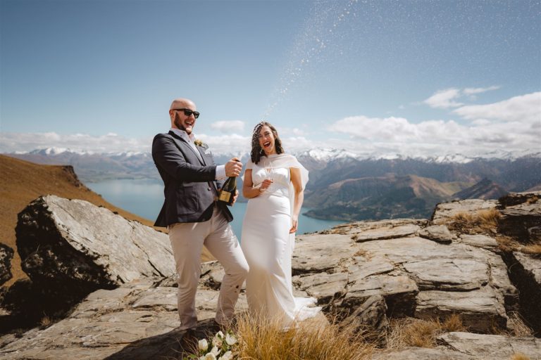 Bride and groom celebrating their wedding by spraying champagne on mountain top in Queenstown