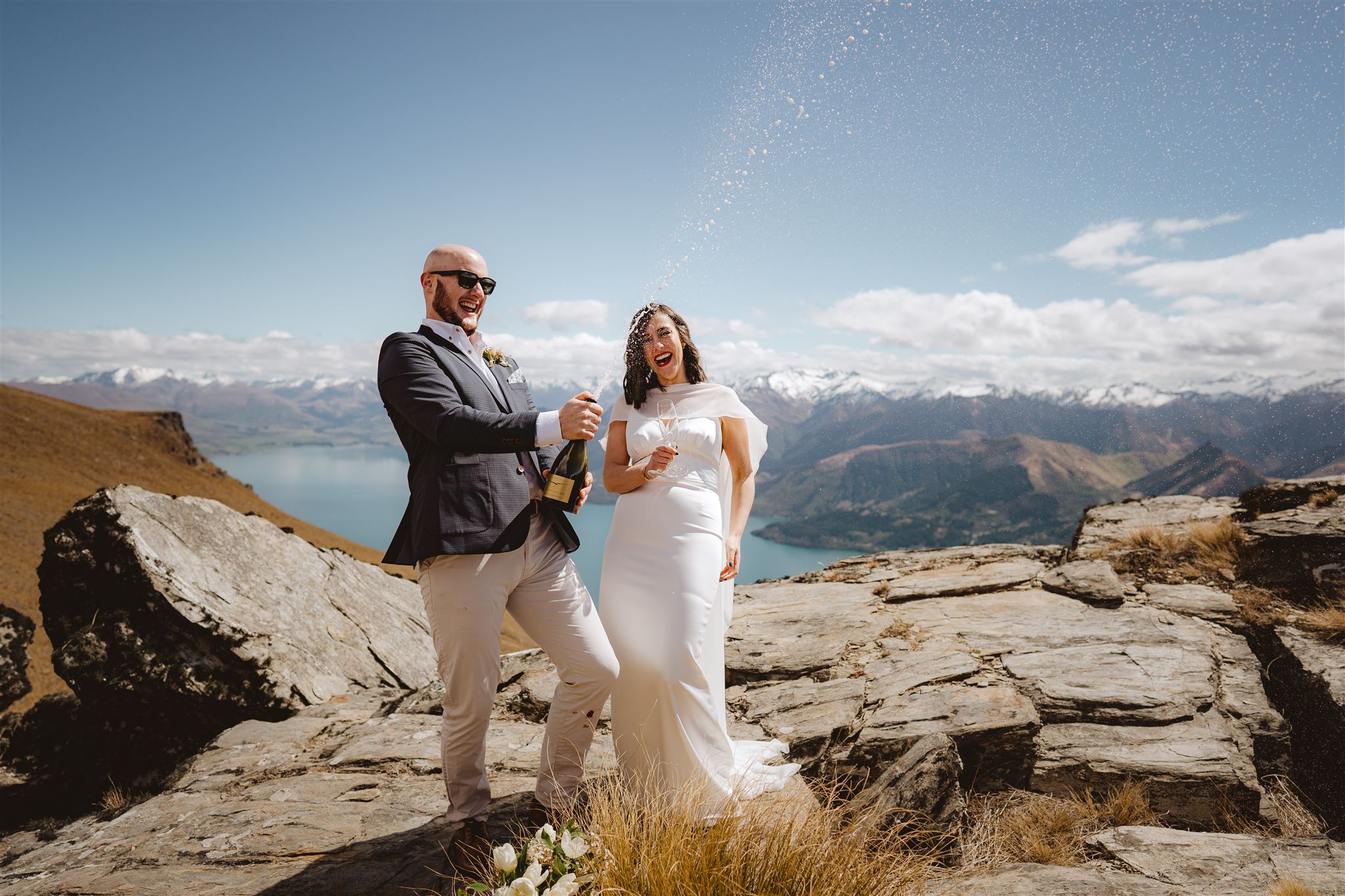 Bride and groom pop champagne on mountain top in Queenstown after their wedding ceremony