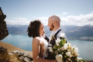 Bride and groom looking into each others eyes on mountain top with Queenstown and Lake Wakatipu in the background