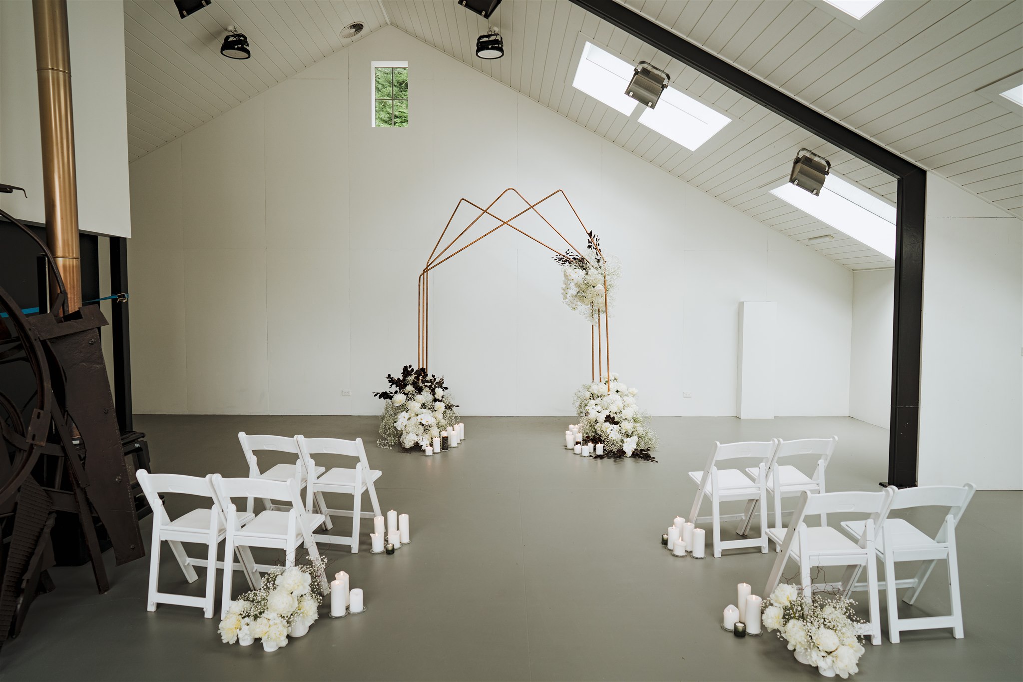indoor Queenstown wedding venue at Giverny Estate with copper wedding arch and white chairs and flowers