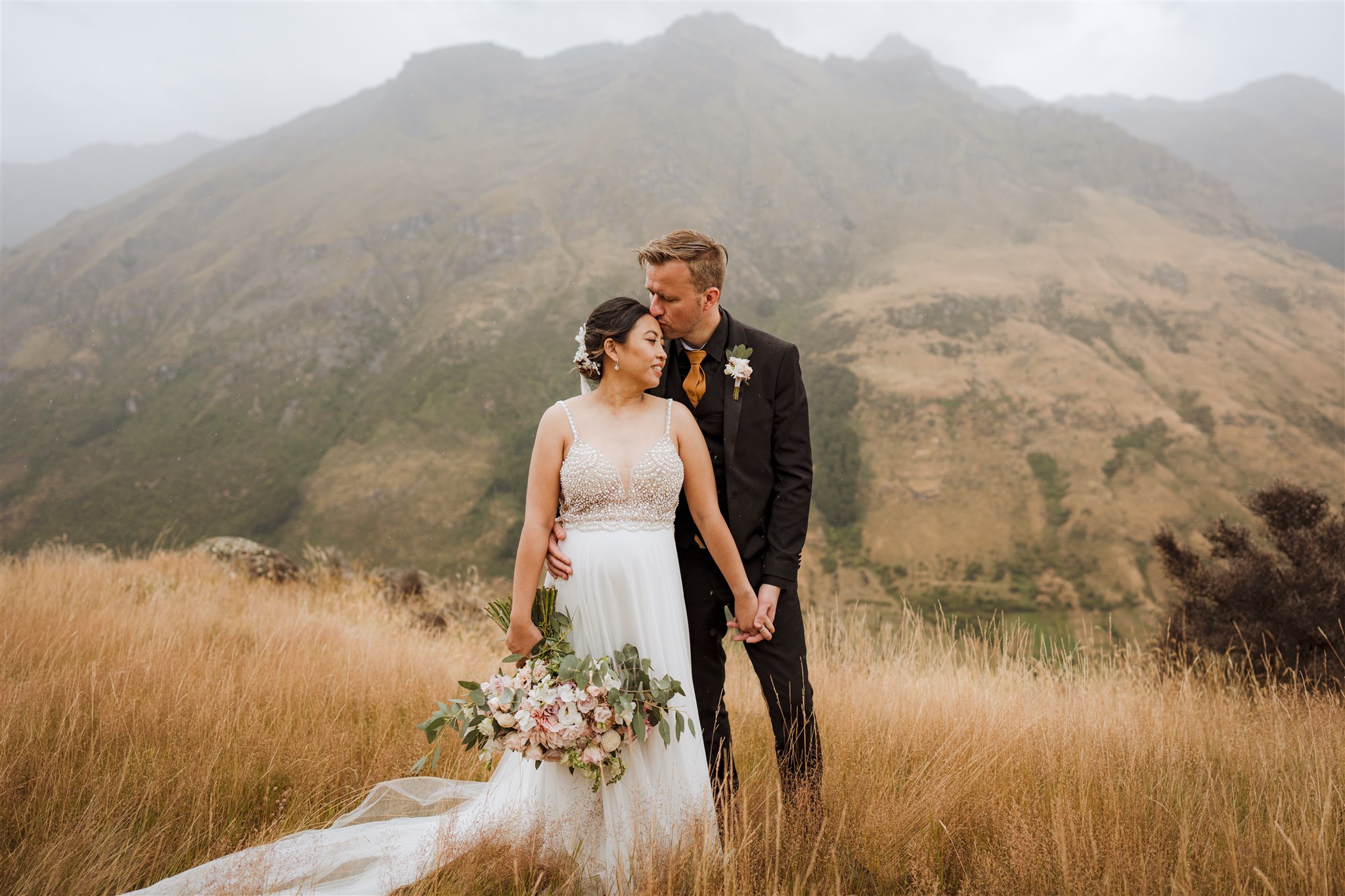 bride and groom pose for wedding photos at Bayonet Peaks in Queenstown New Zealand in the rain