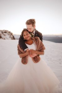 Bride and groom cuddling close on mountain top in the snow at The Remarkables in Queenstown