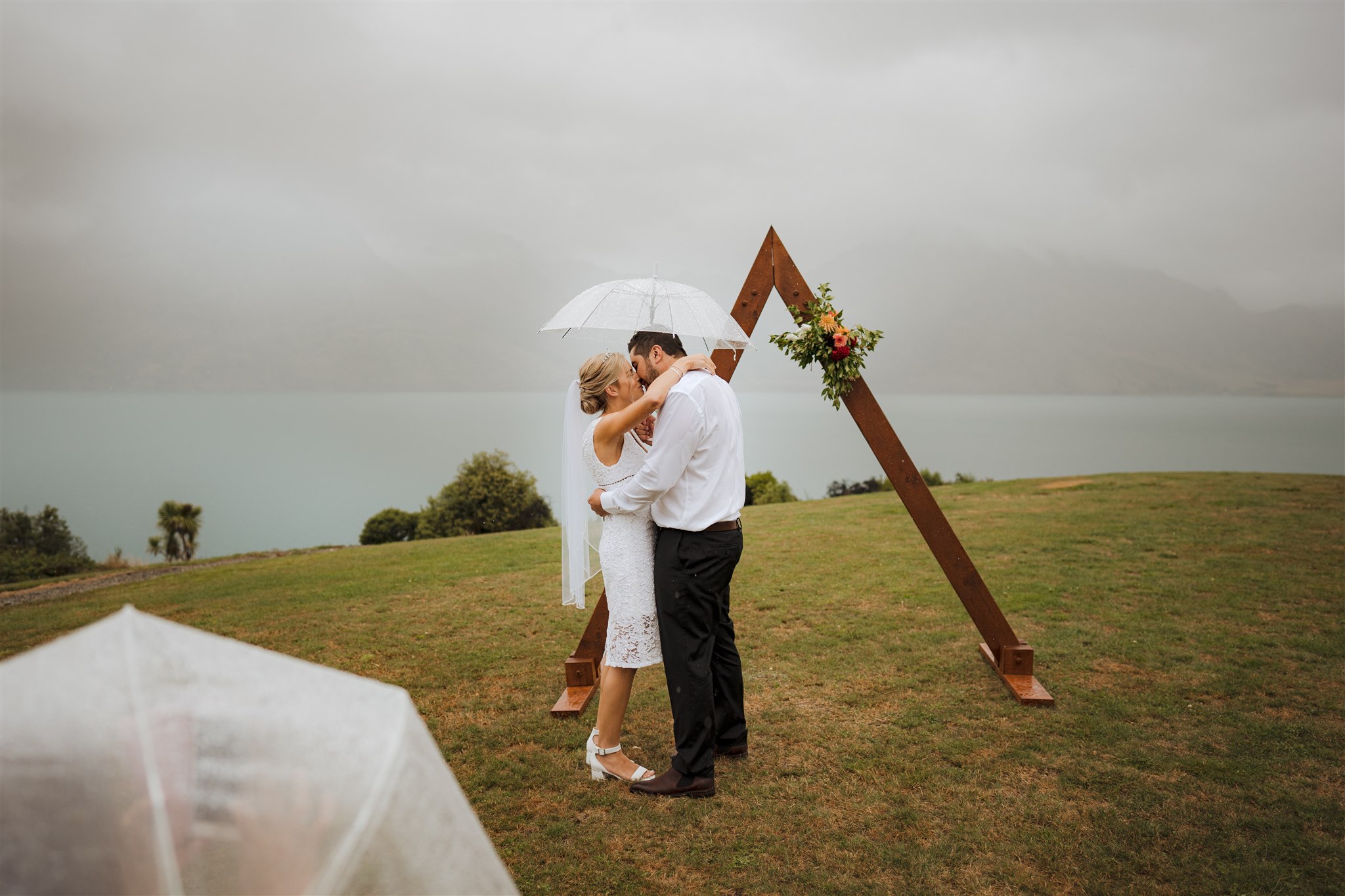 bride and groom kiss under umbrella in the rain during wedding ceremony in queenstown new zealand