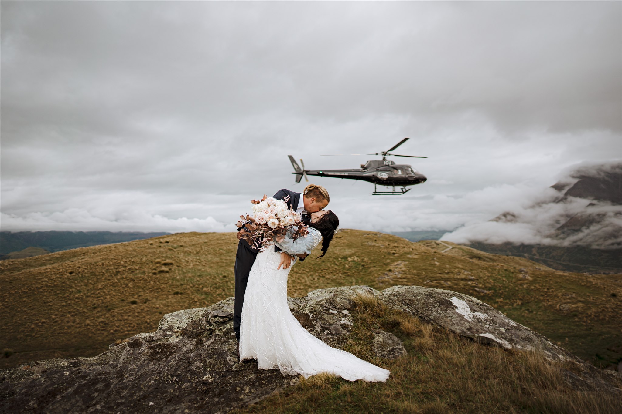 bride and groom kiss as helicopter flies by on their wedding day at Deer Park Heights in Queenstown New Zealand