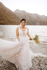 bride plays with dress on the shores of Lochnagar in Queenstown after heli-wedding