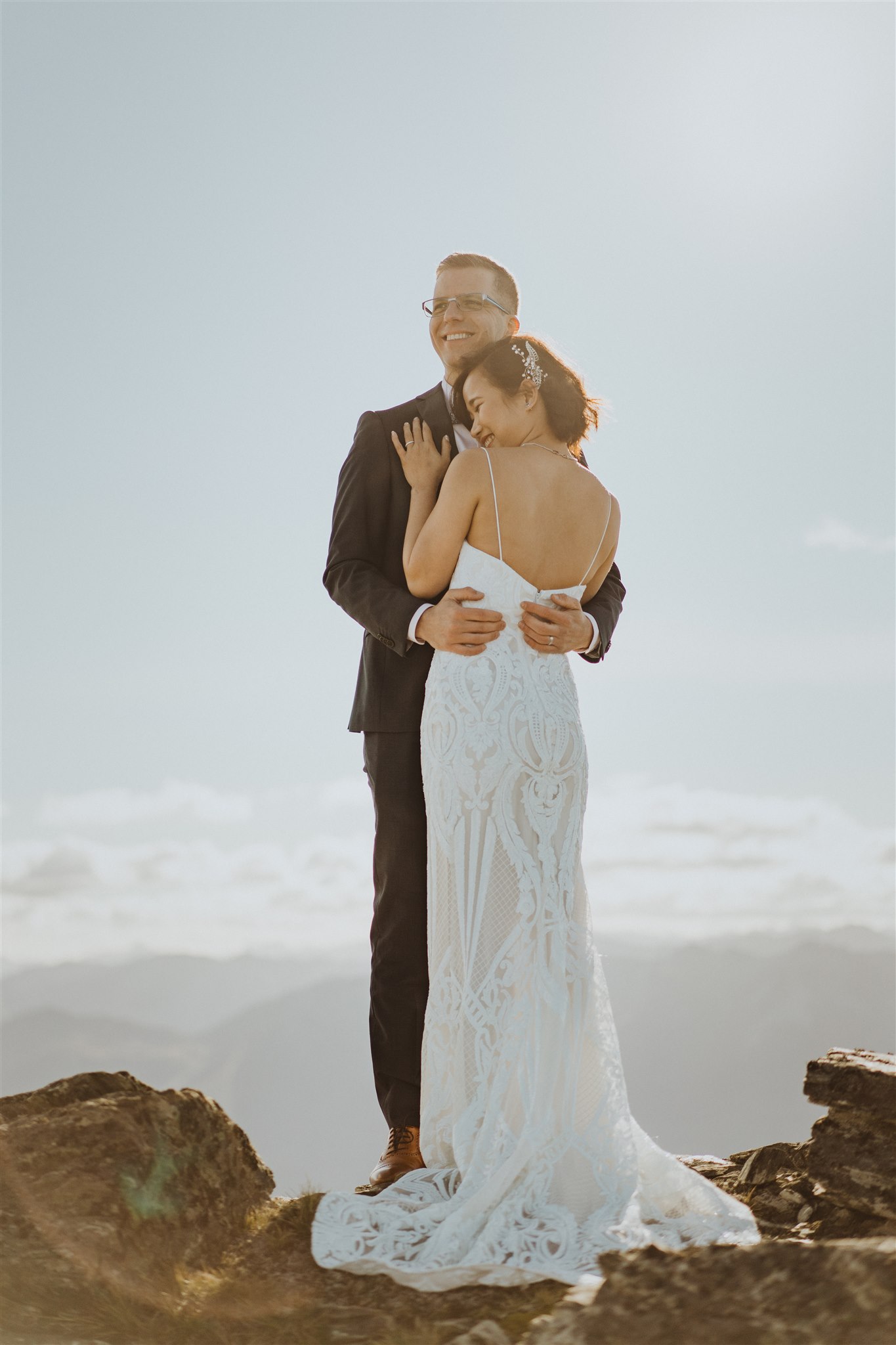 Bride and groom in wedding outfits cuddling on mountain top in Queenstown, New Zealand