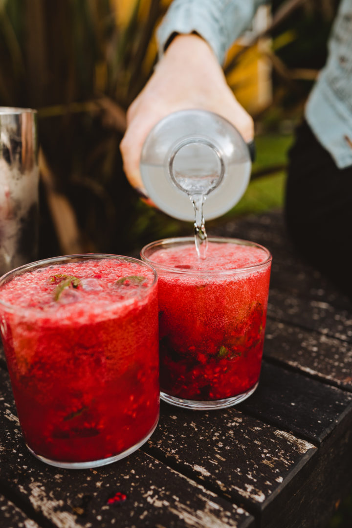 adding sparkling water to raspberry mojito cocktail