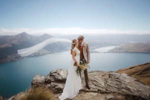 bride and groom on top of a mountain in Queenstown New Zealand with wind blowing veil
