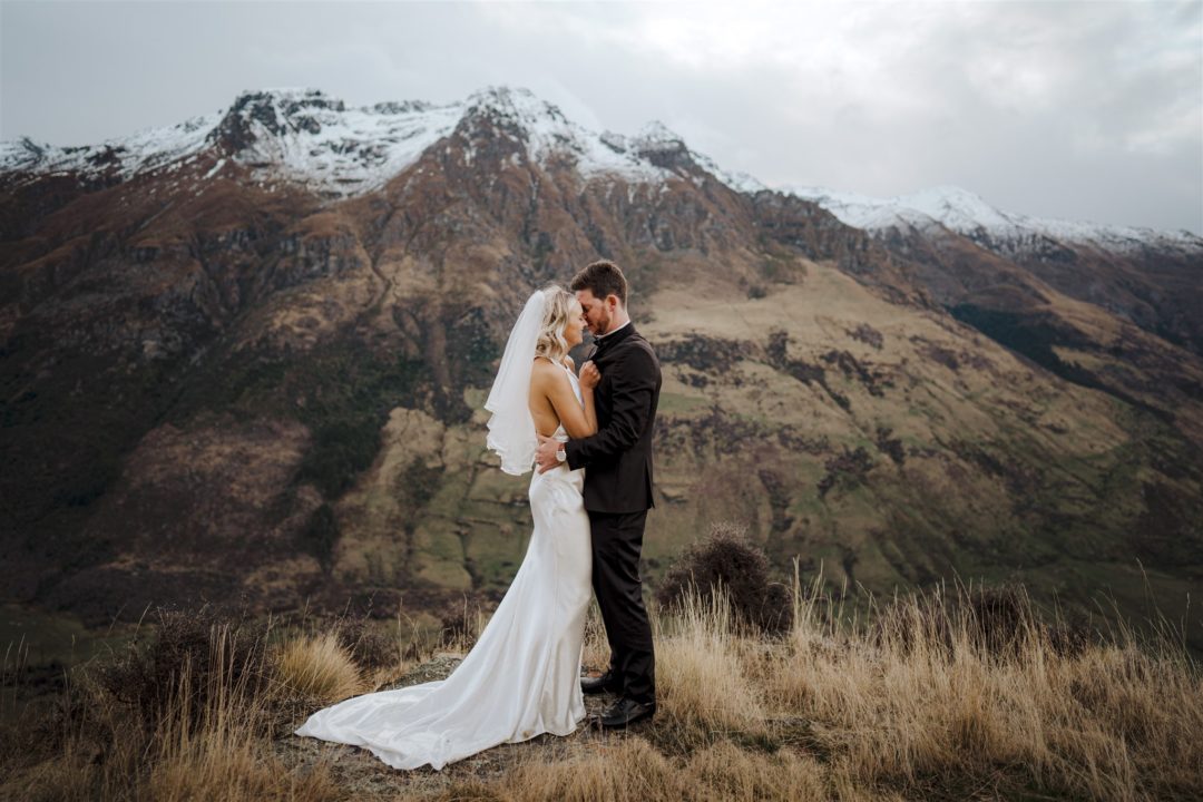 bride and groom hug on a mountain top in Queenstown New Zealand