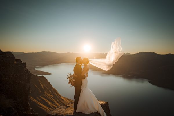 bride and groom kiss and cuddle on top of mountain at sunset after Queenstown helicopter wedding in New Zealand