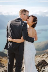 bride and groom cuddle on top of mountain at Mount Crichton in Queenstown New Zealand