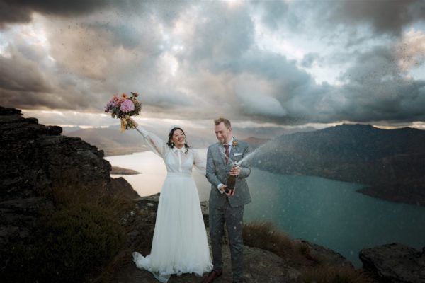 Bride and groom pop champagne and celebrate on Cecil Peak in Queenstown New Zealand